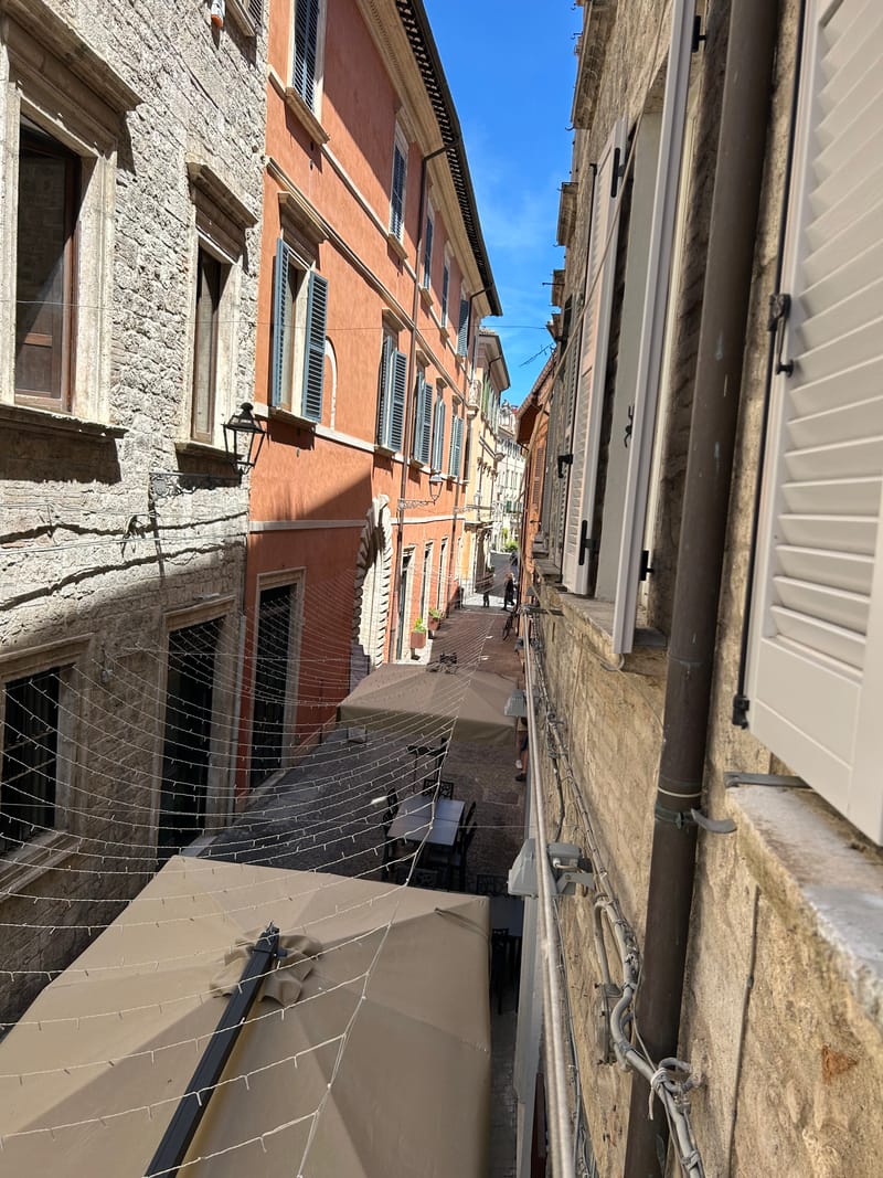 Affaccio dalla finestra su un vicolo di Ascoli, tra facciate in pietra e persiane